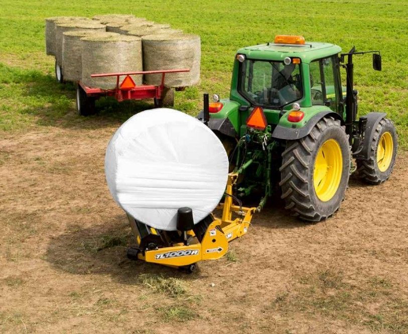 A green tractor is pulling a trailer full of hay bales.