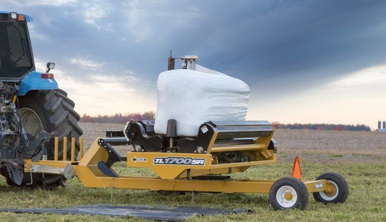 A tractor is wrapping a bale of hay in a field.