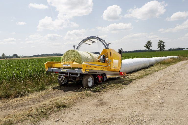 A large bale of hay is being wrapped in plastic on a trailer.