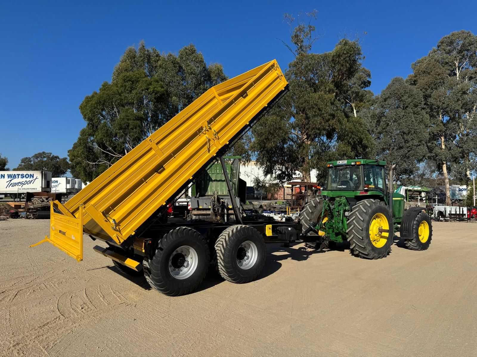 A yellow trailer with a john deere tractor in the background