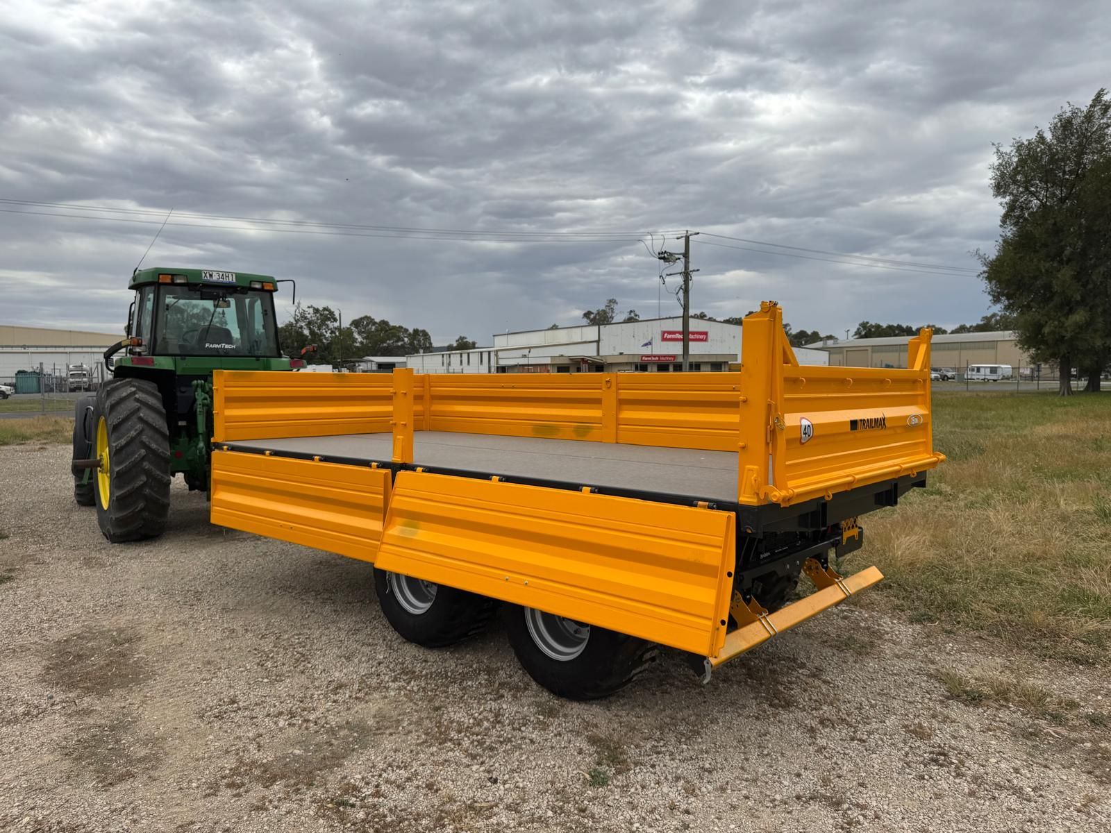 A yellow trailer is attached to a tractor in a dirt field.
