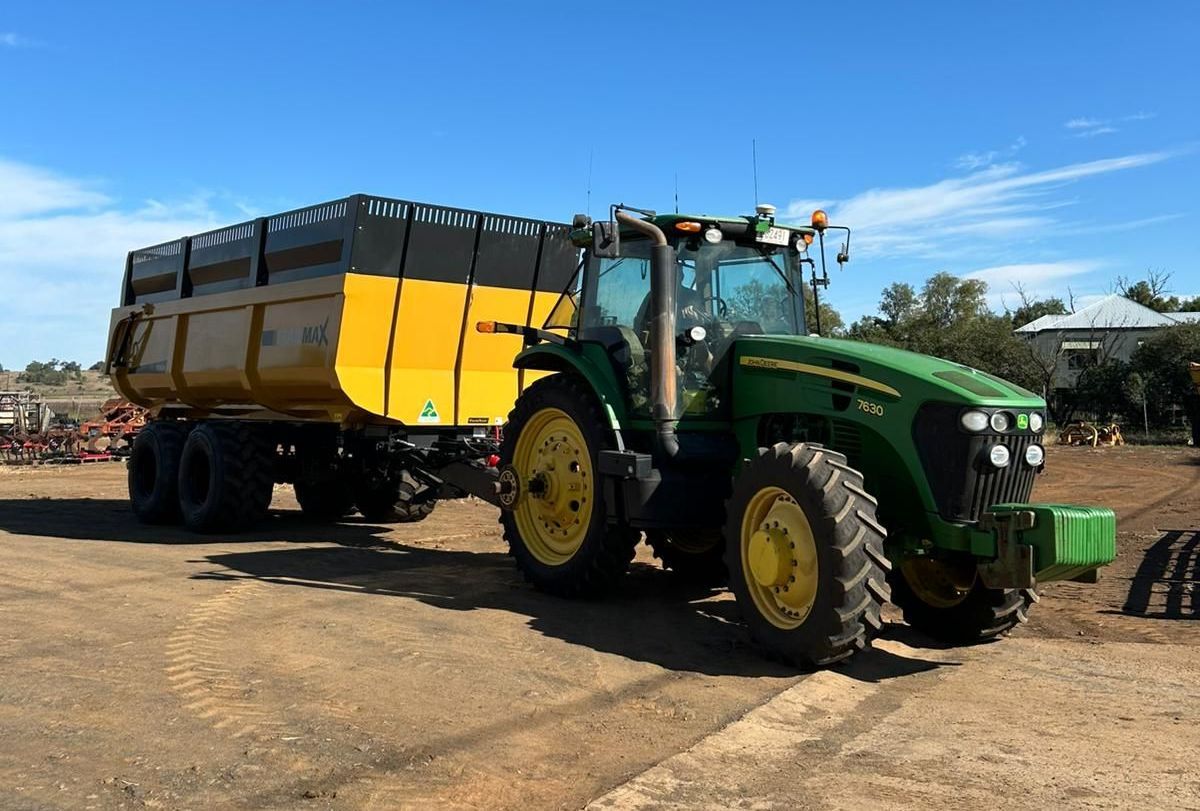 A yellow trailer is attached to a tractor in a dirt field.
