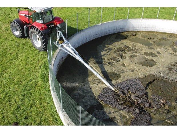 A red tractor is pumping dirt into a large tank