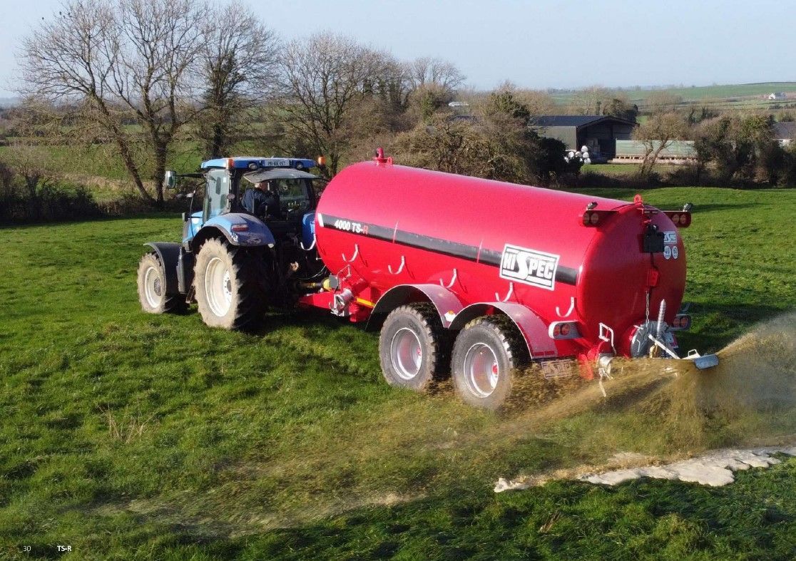 A tractor is pulling a red slurry tanker through a grassy field.