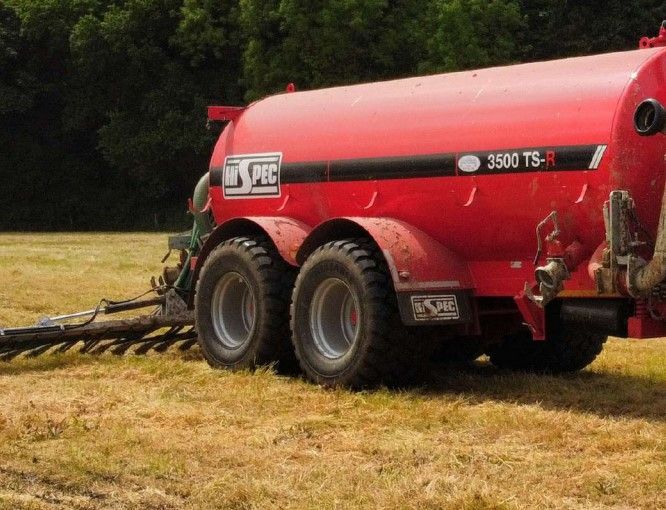A red slurry tanker truck is parked in a field.