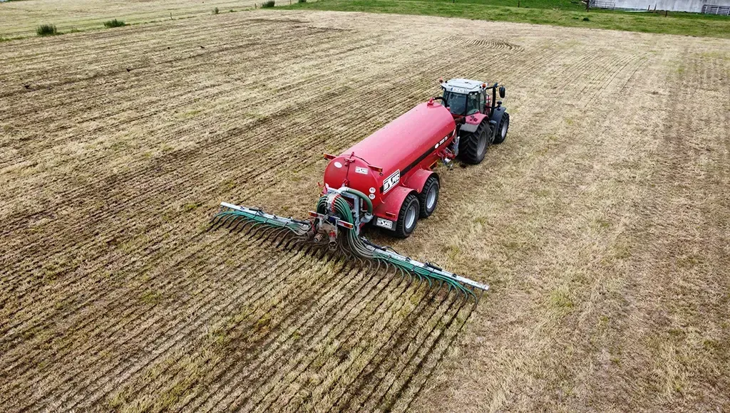 An aerial view of a red slurry tanker spraying a field.