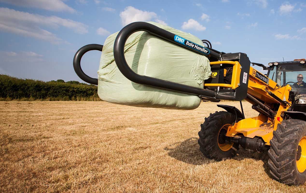 A yellow tractor is carrying a large bale of hay in a field.