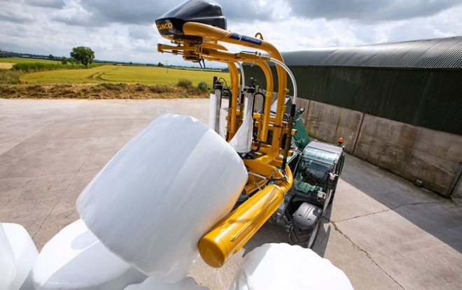 A yellow and white machine is wrapping a bale of hay.