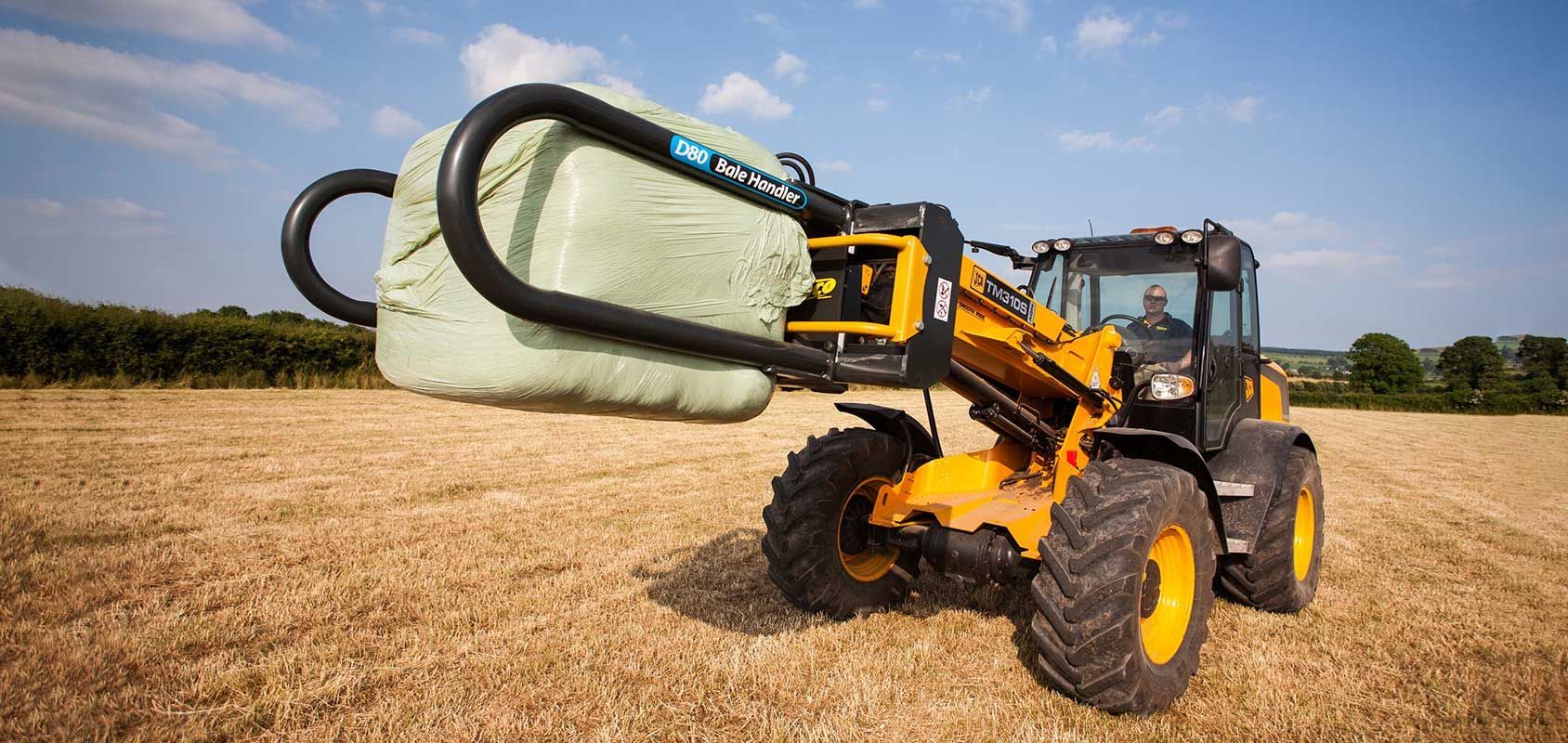 A yellow tractor is carrying a bale of hay in a field.