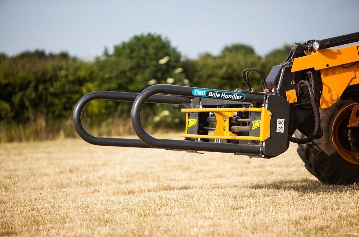 A yellow tractor is parked in a field with a forklift attached to it.