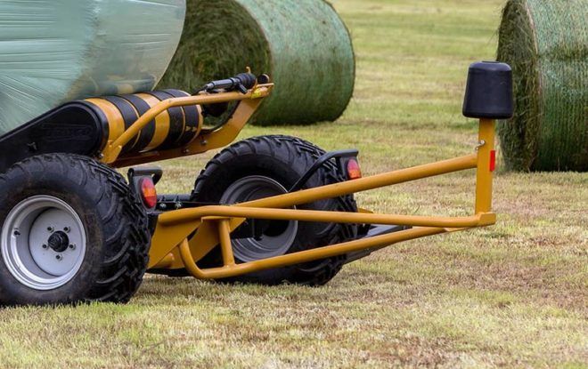 A tractor is wrapping hay bales in plastic in a field.