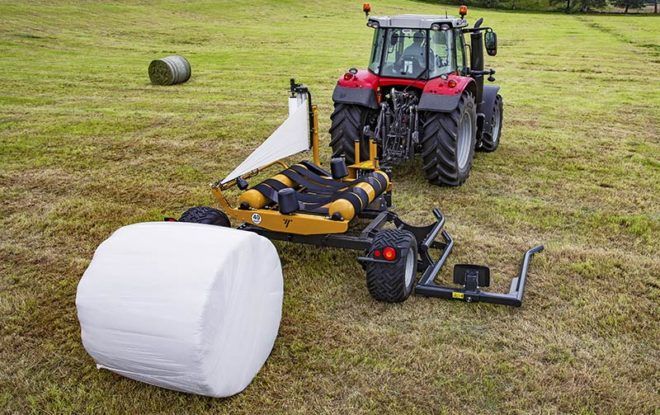 A tractor is wrapping a bale of hay in a field.