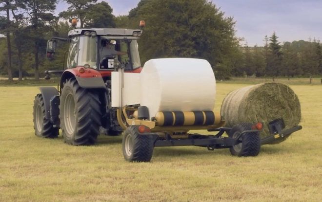 A tractor is wrapping hay bales in a field