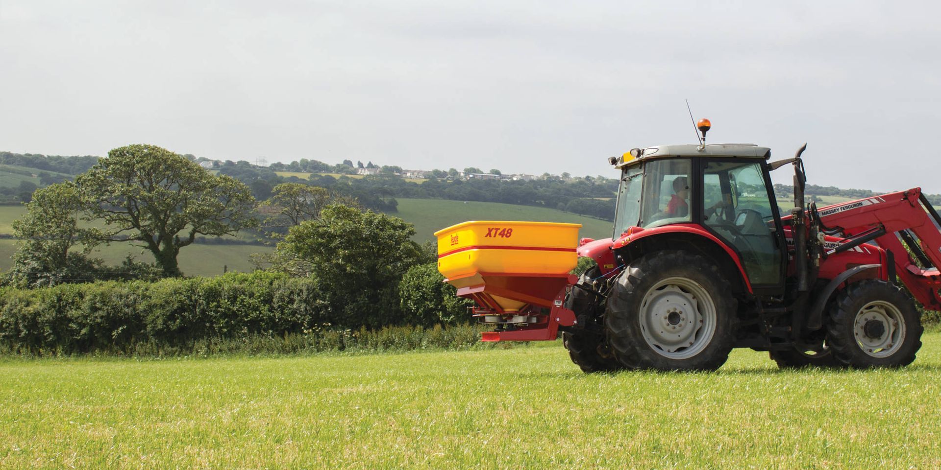 A red tractor is spreading fertiliser in a field.