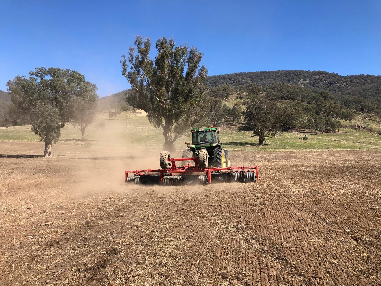 A red tractor is plowing a field with a trailer attached to it.