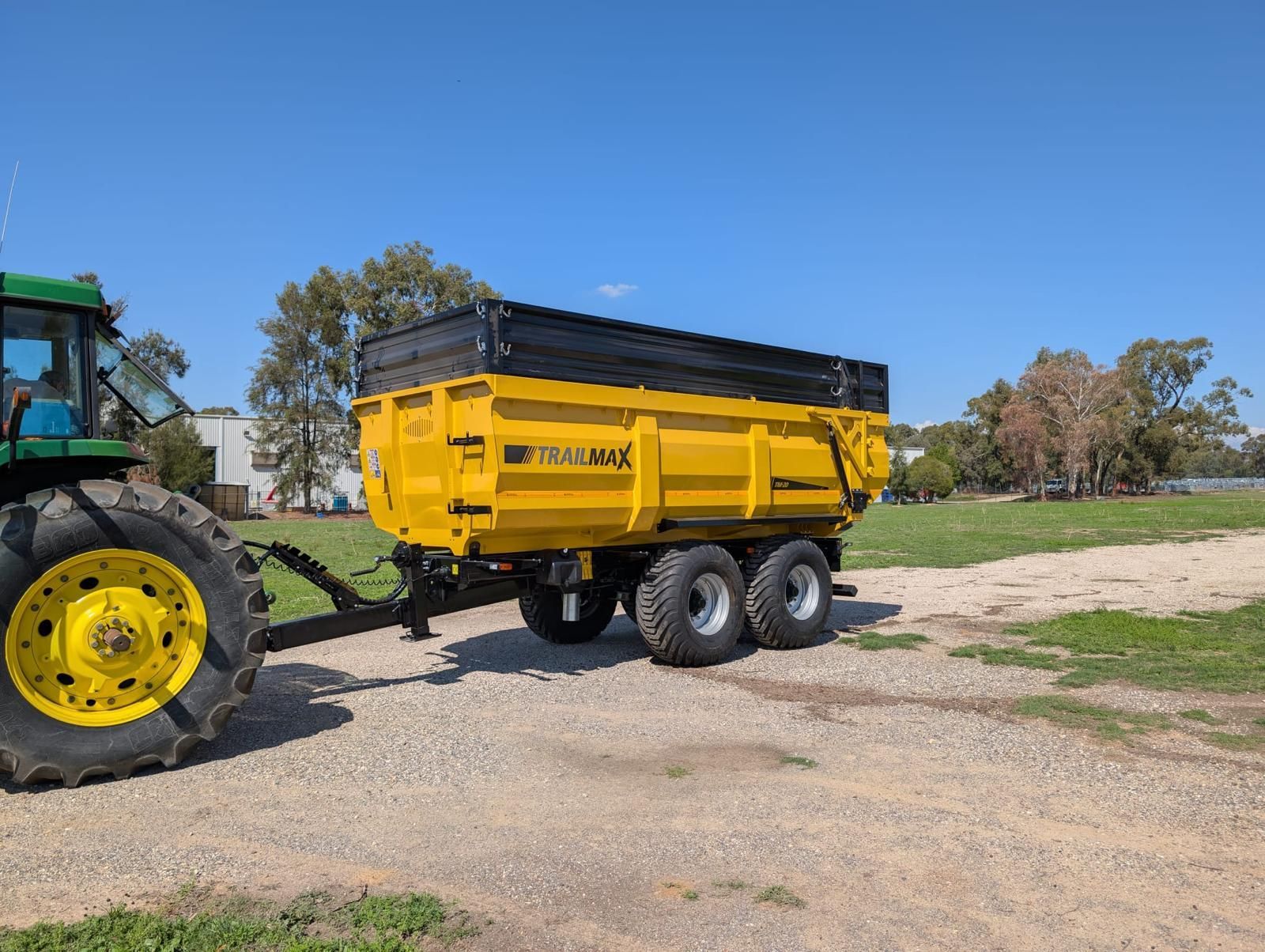 A green tractor is pulling a yellow trailer on a dirt road.