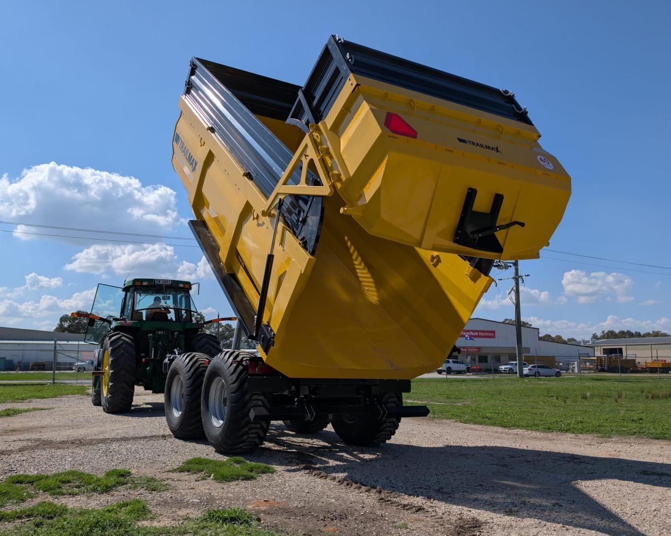 A yellow dump truck is parked next to a tractor in a dirt field.