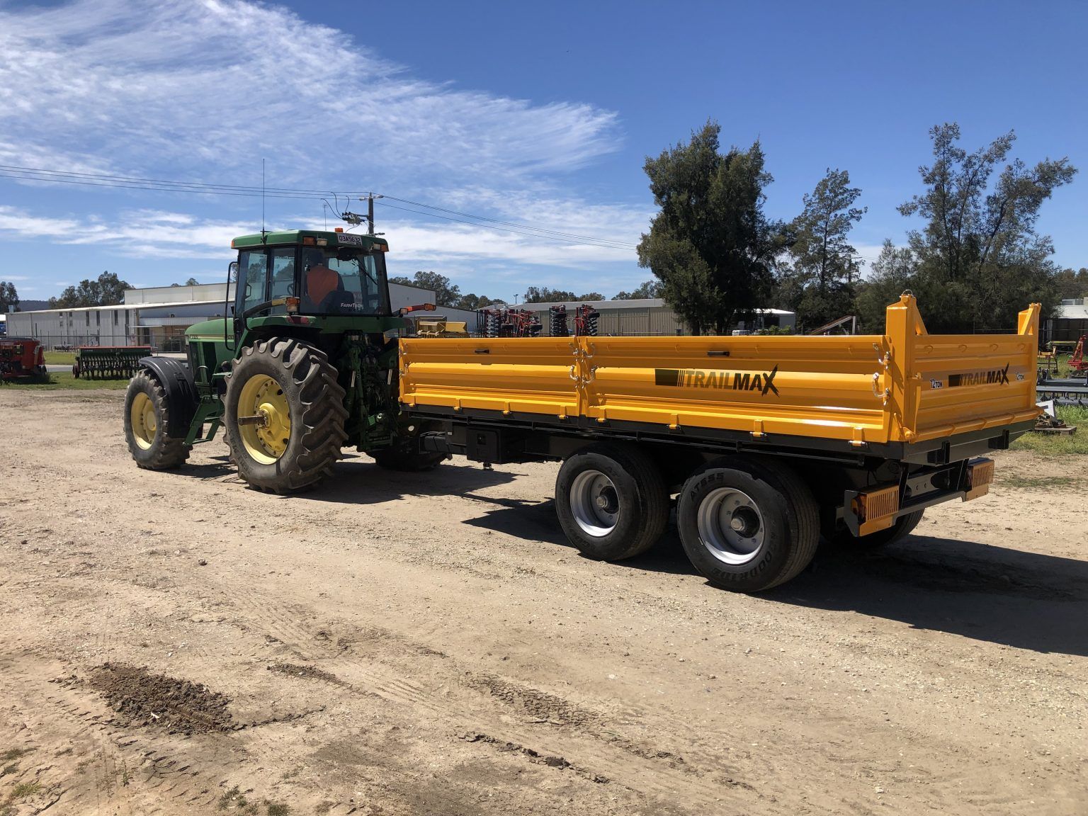 A green tractor is pulling a yellow trailer on a dirt road.