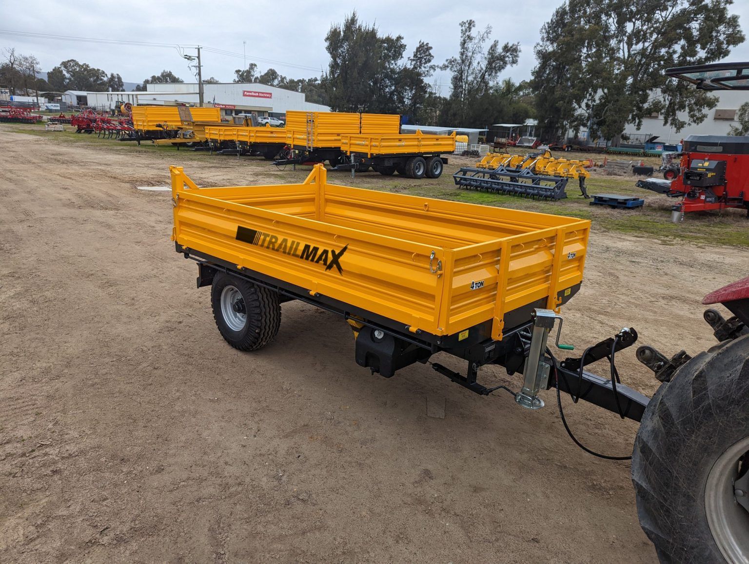 A yellow trailer is attached to a tractor in a dirt field.