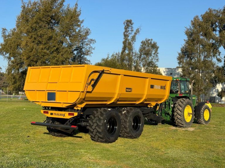 A yellow silage trailer is pulled by a green tractor