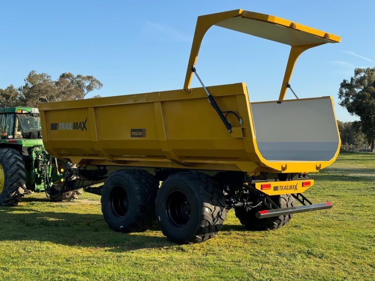A yellow silage trailer is parked next to a green tractor in a grassy field.