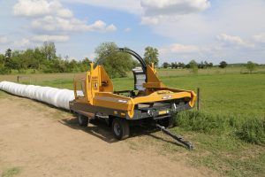A yellow and black machine is wrapping hay bales in a field.