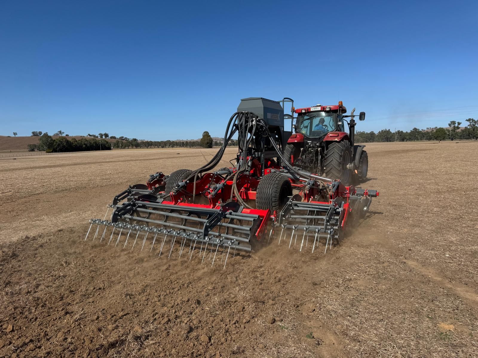 A red and gray disc tiller is parked in a grassy field.