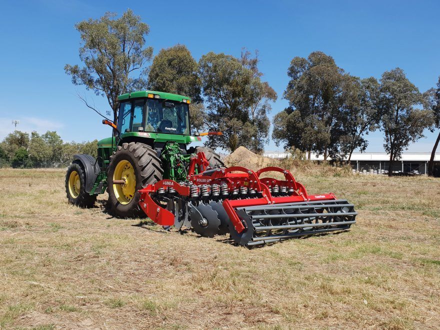 A green john deere tractor is parked in a field with a disc tiller