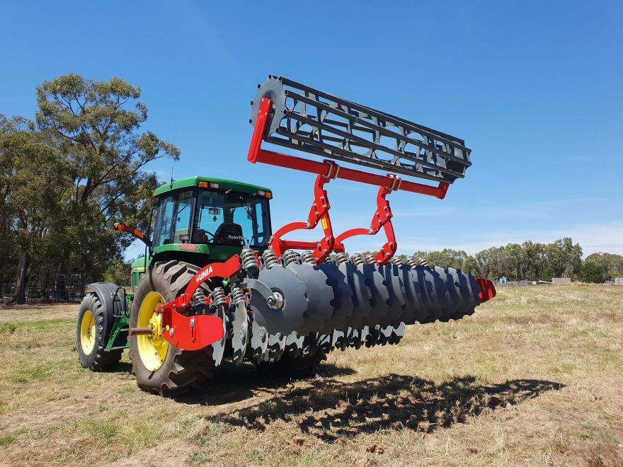 A john deere tractor is driving through a dry grass field with a disc tiller