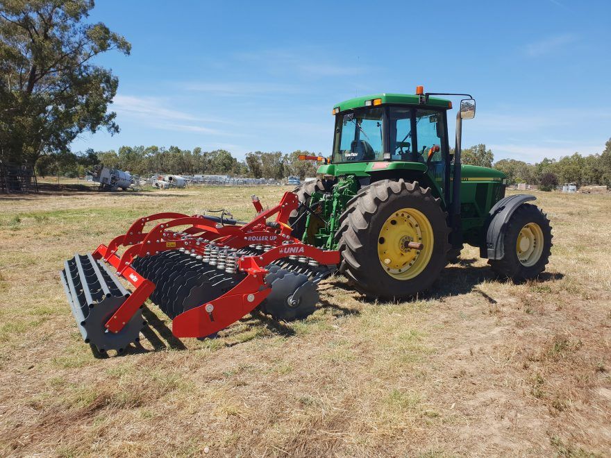 A green john deere tractor is parked in a field with a disc tiller