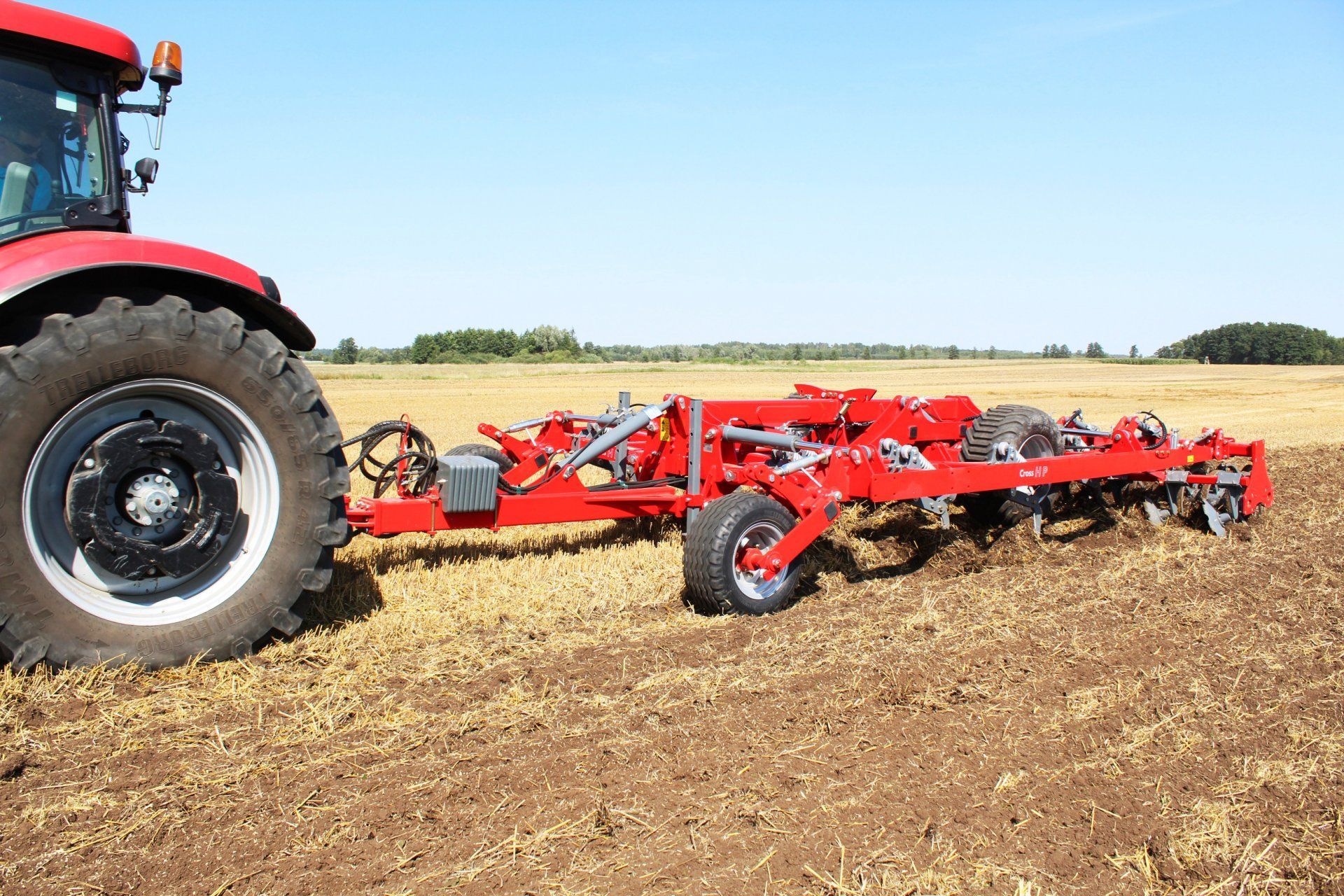 A red tractor is plowing a field with a trailer attached to it.