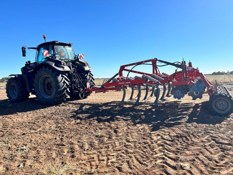 A black and red tractor is pulling a large machine in a dirt field