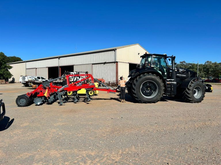 A black tractor is towing a red and yellow tractor in a parking lot.