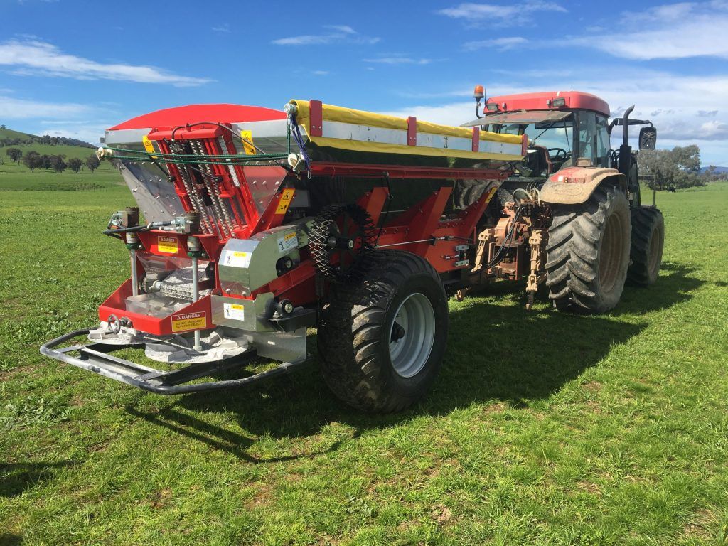 A tractor is parked in a grassy field with a spreader attached to it.