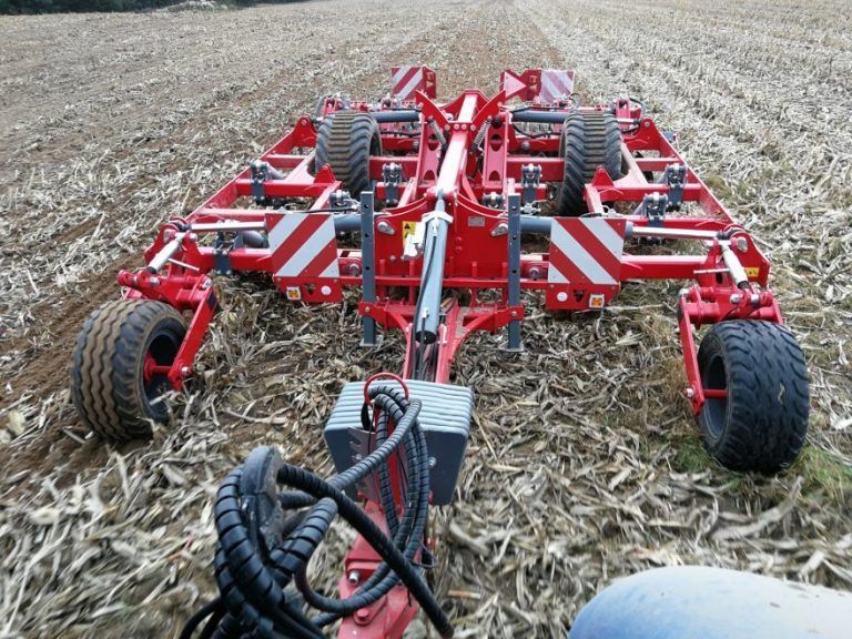A red and white disc tiller is parked in a field