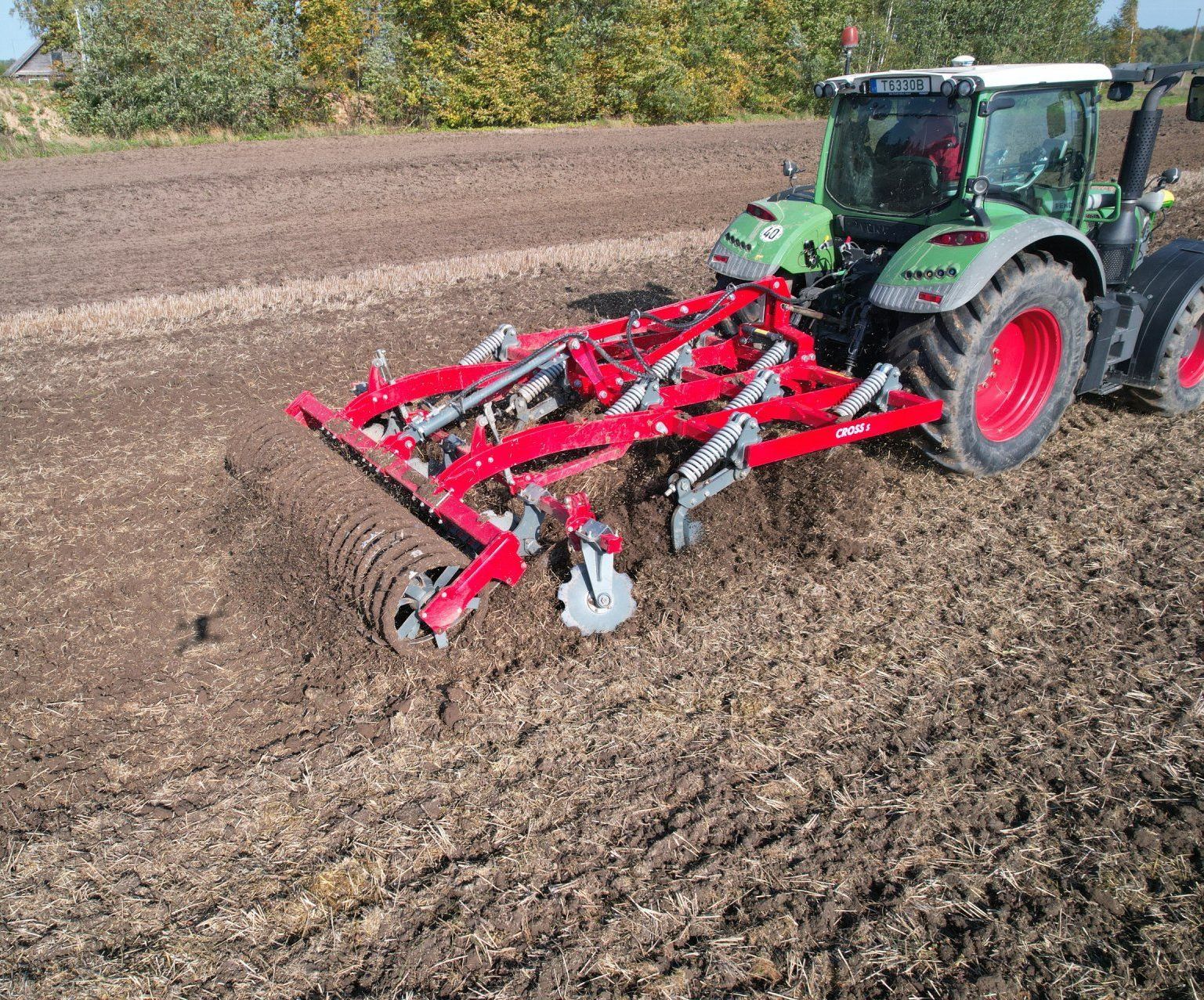 A tractor is plowing a field with a disc tiller attached to it.