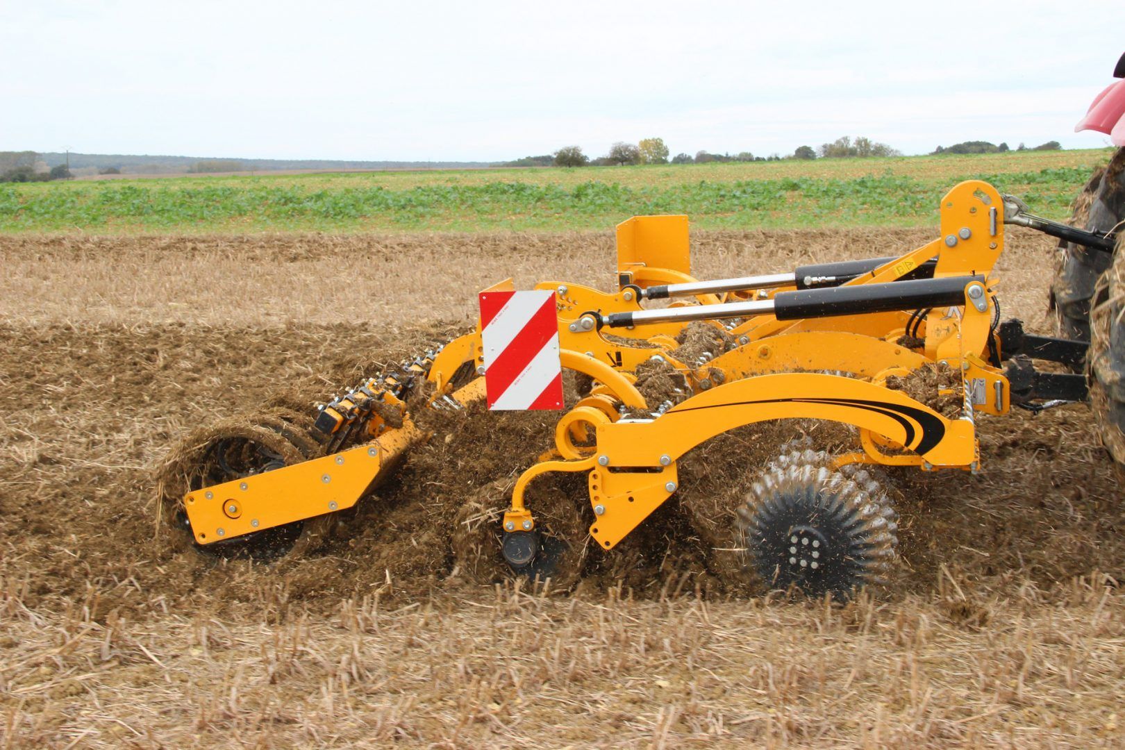 Side view of a yellow disc tiller in a field.