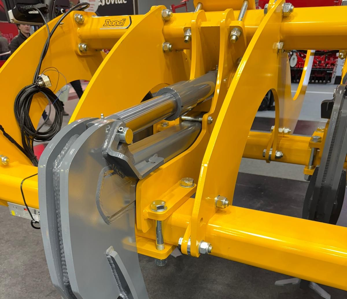 A yellow and gray machine is sitting next to a green tractor.