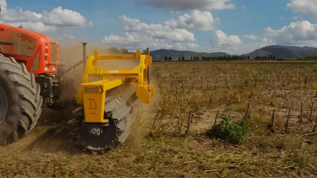 A tractor is plowing a field with a yellow machine.