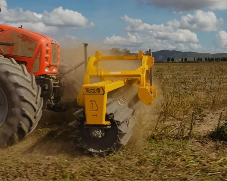A yellow tractor is plowing a field with mountains in the background