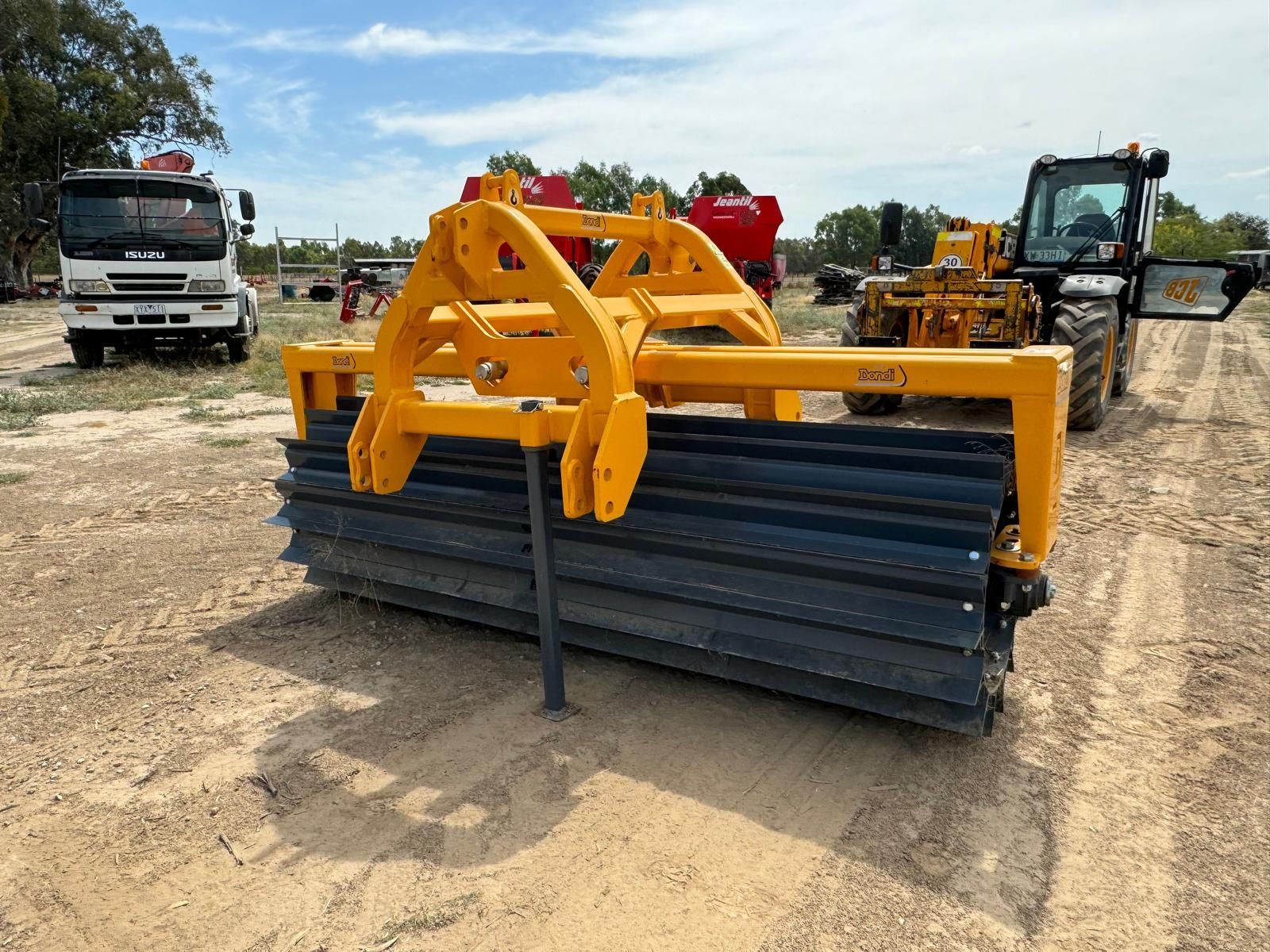 A yellow and blue tractor is parked in a dirt field next to a truck.