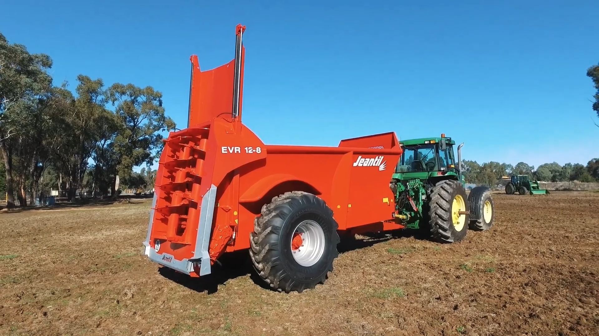 A red tractor is parked in a field next to a green tractor.