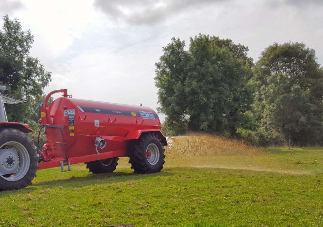 A red tractor is driving through a grassy field.