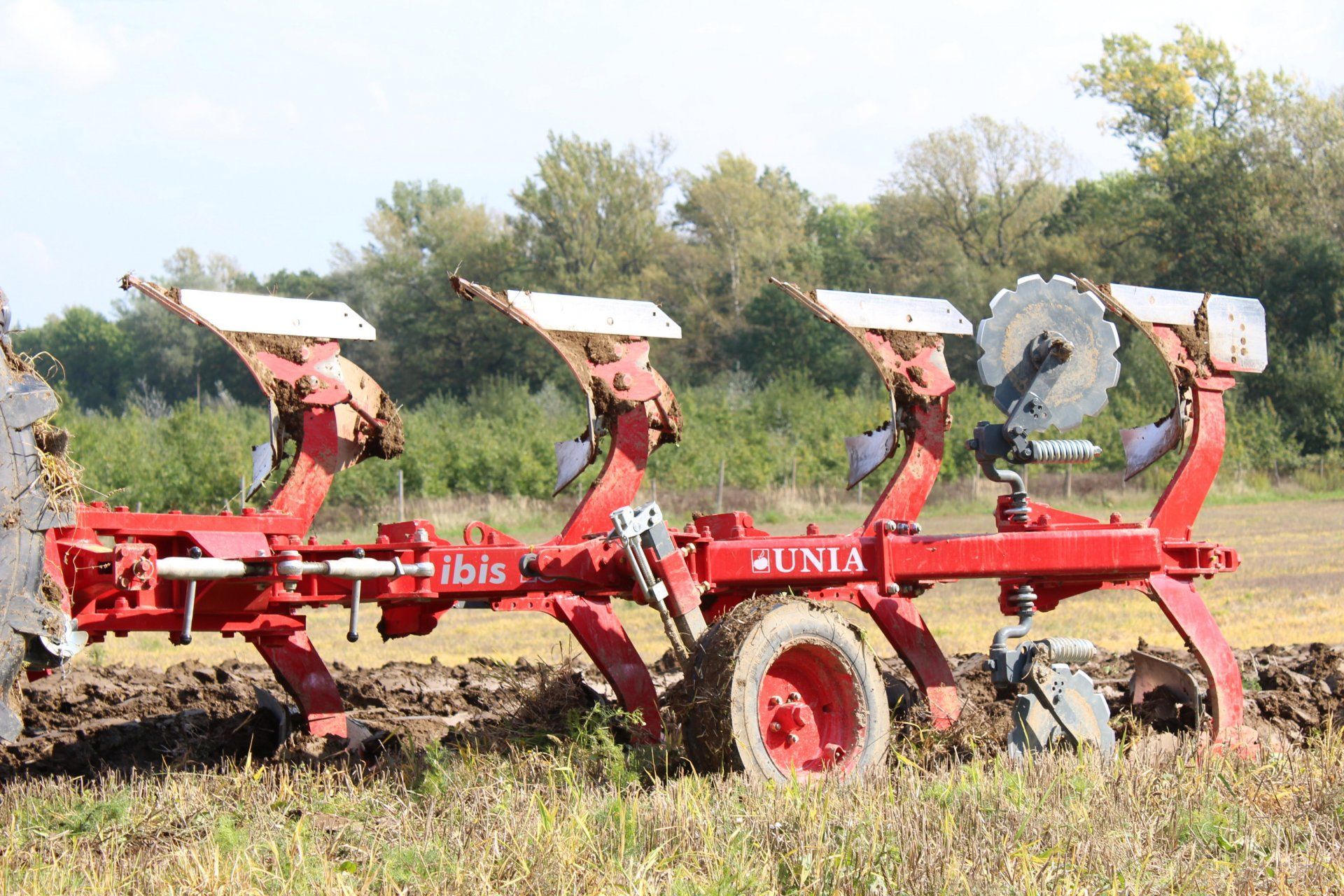A red tractor is plowing a field with a trailer attached to it.