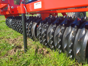 A close up of a machine in a field with a tractor in the background.