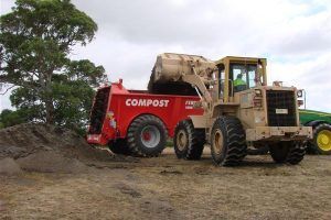 A red manure spreader is being loaded with dirt by a front end loader.