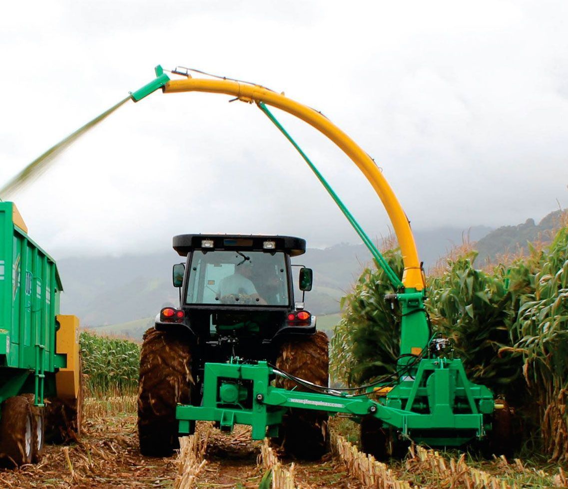 A tractor is cutting grass in a field with a machine attached to it.