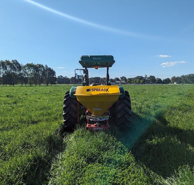 A yellow spreader is on the back of a tractor in a grassy field