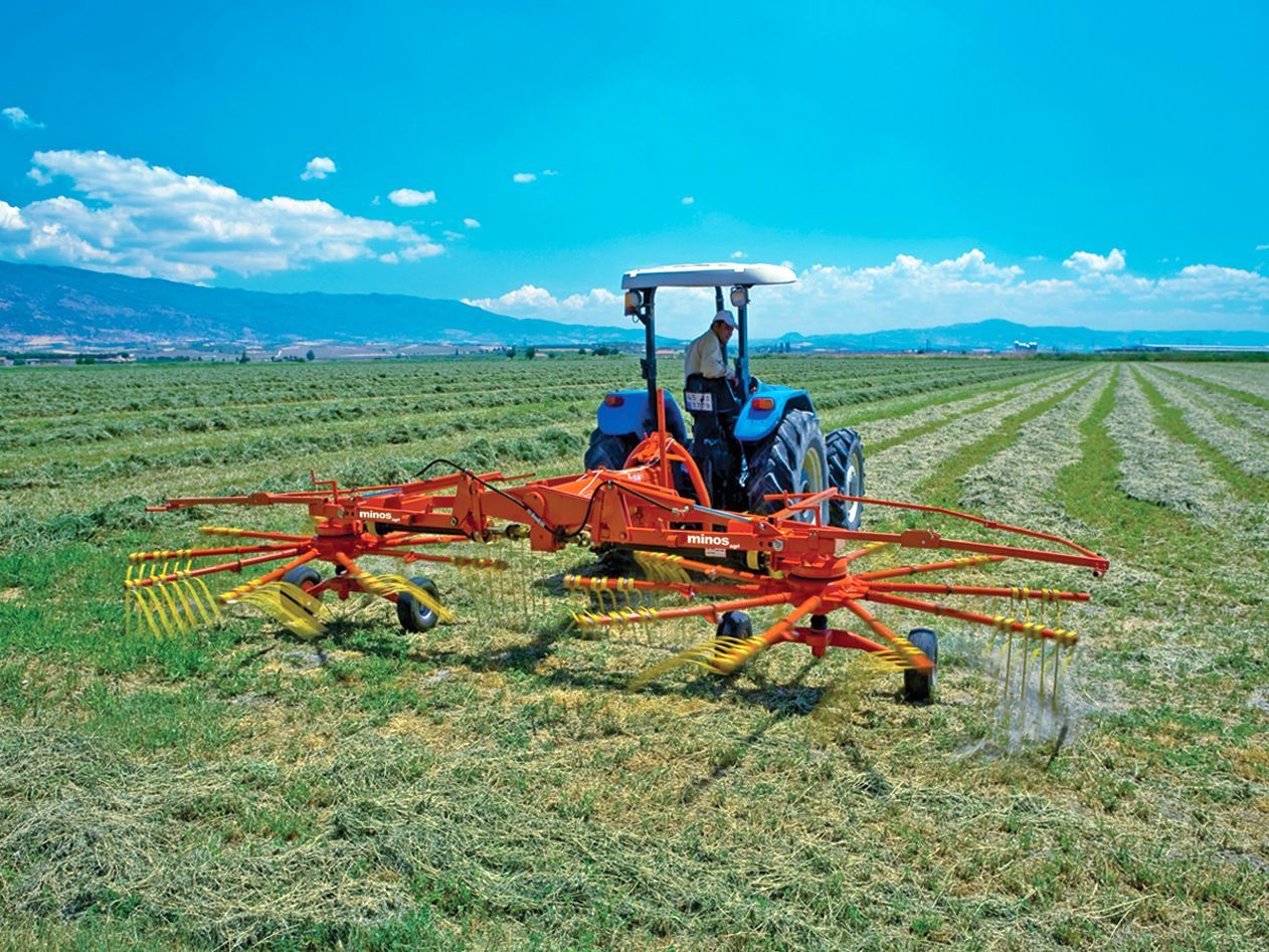 A man is driving a tractor through a field of hay.