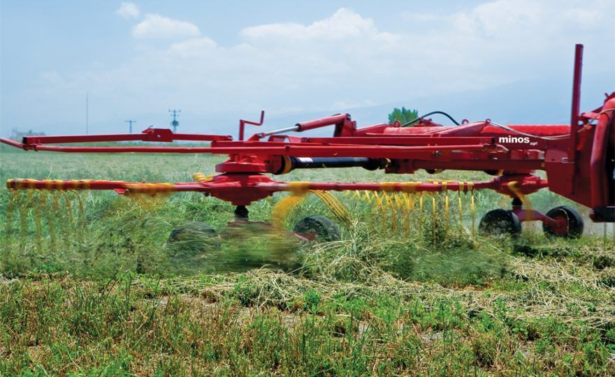 A red and yellow tractor is cutting grass in a field.